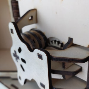 May include: Close-up of a wooden box with a complex gear mechanism. The gears are made of wood and are visible through a cutout in the box. The mechanism is designed to open the box.