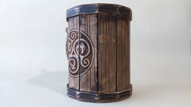May include: A wooden mug with a Celtic knot design carved into the side. The mug is brown and has a dark brown rim.