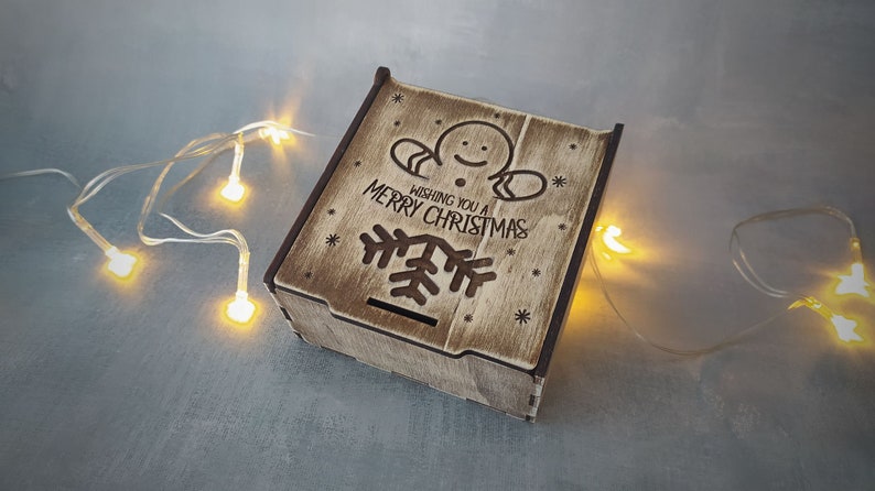 May include: A wooden box featuring a gingerbread man design and the text "Wishing you a Merry Christmas". The box is decorated with snowflakes and a Christmas tree.