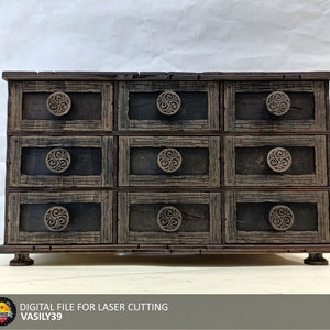 Könnte beinhalten: Eine Holzkiste mit neun Schubladen, jede mit einem dekorativen, runden Knopf im keltischen Knotendesign. Die Kiste ist dunkelbraun und hat ein rustikales, antikes Aussehen.