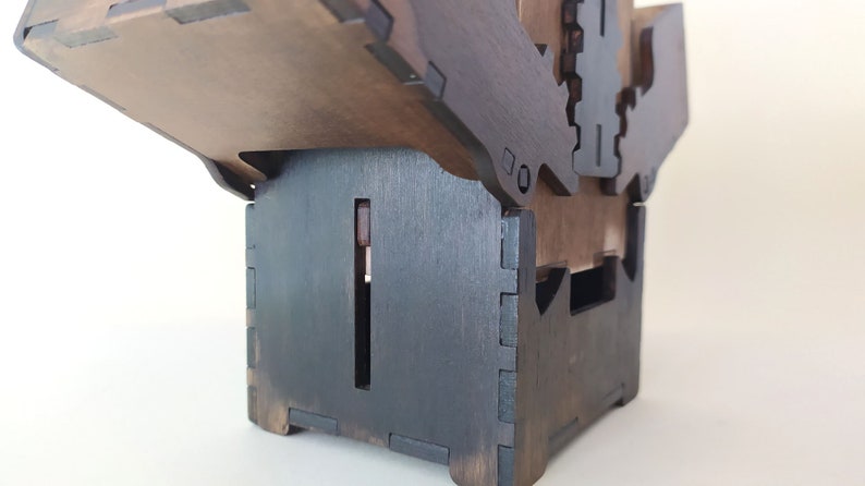 May include: A dark brown wooden box with a hinged lid. The box is made of multiple pieces of wood that are joined together with a dovetail joint. The box has a small opening on the side.