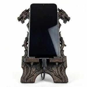 May include: A dark brown wooden phone stand with a dragon design. The stand holds a black smartphone, with a charging cable connected. The stand features two dragon heads at the top and intricate carvings.