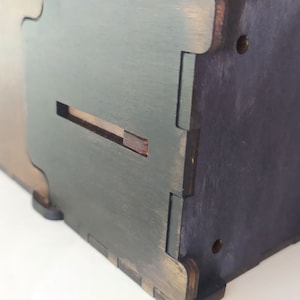May include: A wooden box with a slot on the side. The box is painted in a dark green color and has a brown wood grain finish.