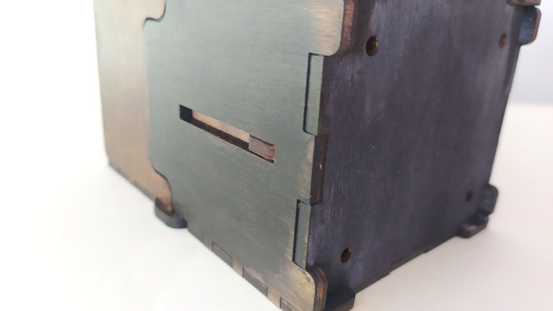 May include: A wooden box with a slot on the side. The box is painted in a dark green color and has a brown wood grain finish.