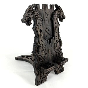 May include: A dark brown wooden phone stand with a dragon head design. The stand features carved details, including runes and a vine-like pattern. The stand is designed to hold a phone and has a unique, artistic aesthetic.