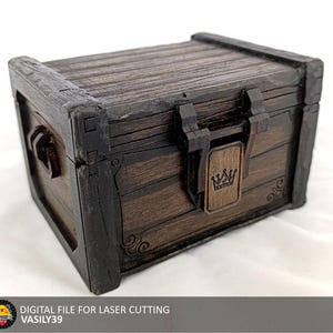 May include: A wooden treasure chest with a dark brown finish and black trim. The chest features a crown emblem on the latch and decorative scrollwork. The text "DIGITAL FILE FOR LASER CUTTING" and "VASILY39" are visible.