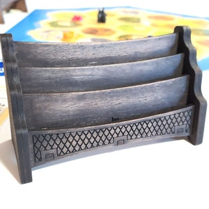 May include: A dark brown wooden card holder with three slots. The holder has a decorative design on the bottom.