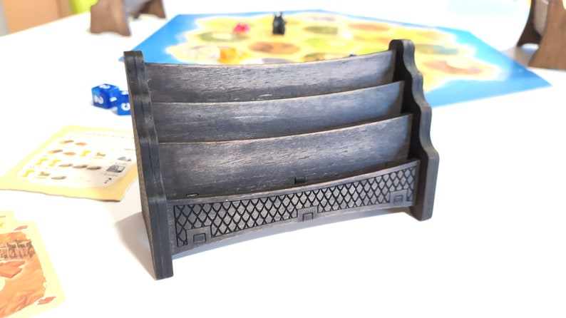 May include: A dark brown wooden card holder with three slots. The holder has a decorative design on the bottom.