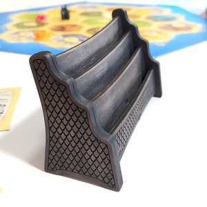 May include: A black wooden card holder with three slots. The holder has a decorative pattern on the sides.