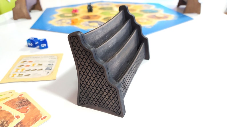 May include: A black wooden card holder with three slots. The holder has a decorative pattern on the sides.