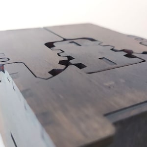 May include: A dark wooden box with a unique interlocking design. The box has a hinged lid and a detailed cutout pattern on the top.