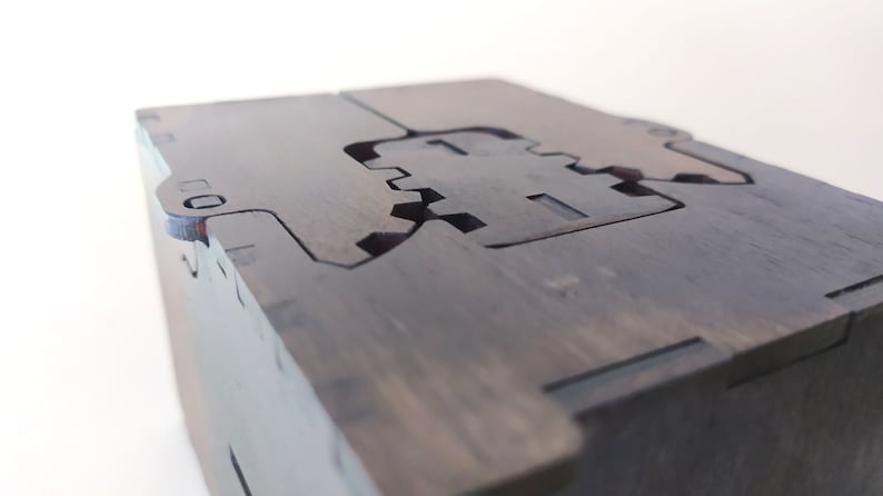 May include: A dark wooden box with a unique interlocking design. The box has a hinged lid and a detailed cutout pattern on the top.