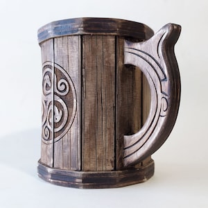 May include: A wooden beer stein with a dark brown finish and a carved handle. The stein features a circular design with a Celtic knot pattern.