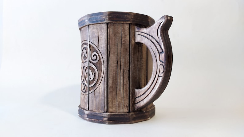 May include: A wooden beer stein with a dark brown finish and a carved handle. The stein features a circular design with a Celtic knot pattern.