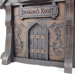 May include: A dark brown wooden structure featuring a central arched door with a keyhole, flanked by two engraved dragon motifs. Above the door, a rectangular sign is clearly inscribed with the text DRAGON'S ROOST in dark lettering.