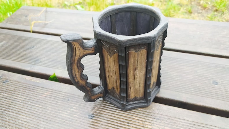 May include: A wooden beer stein with a dark brown finish and a carved handle. The stein has a hexagonal shape and is decorated with intricate carvings.