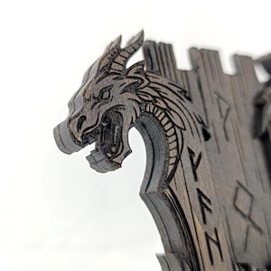 May include: A dark wooden dragon-themed decorative item. The dragon's head is intricately carved with open mouth and detailed features. The item has a castle-like structure with engraved runes. The overall design is a blend of fantasy and craftsmanship.