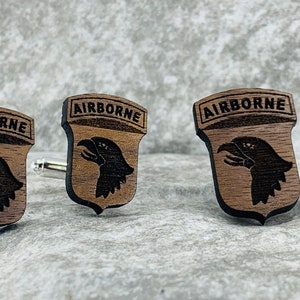 May include: A set of three wooden cufflinks featuring a brown eagle head with the word "AIRBORNE" above it. The cufflinks are made of dark wood and have a polished finish.