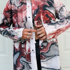 May include: A long-sleeved button-up shirt with a white base and a red, black, and gray marbled pattern.