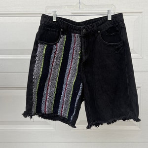 May include: Black denim shorts with a colorful sequined panel on the left side. The shorts have a frayed hem and a distressed look.