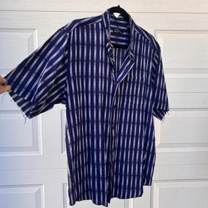 May include: A blue and white striped short-sleeved button-down shirt with a pocket on the left side. The shirt is hanging on a black hanger.