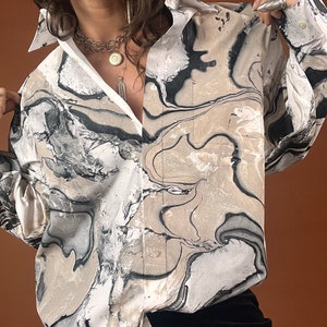 May include: A white button-down shirt with a black and brown marbled pattern. The shirt has a relaxed fit and long sleeves.