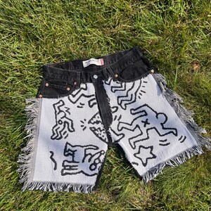 Könnte beinhalten: Schwarze Jeansshorts mit gewebten Paneelen in Weiß und Schwarz mit Figuren im Keith-Haring-Stil. Die Shorts haben einen ausgefransten Saum. Das Etikett lautet "REGULAR".