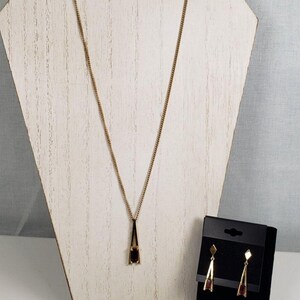 May include: A gold necklace with a pendant featuring a dark red rectangular stone. Matching earrings with the same design are included.