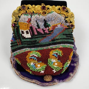 May include: A vintage beaded purse with a gold metal frame and purple stones. The purse is decorated with a colorful beaded design of a landscape with houses and a river.
