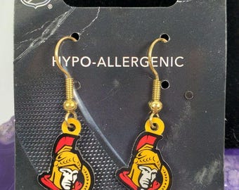May include: A pair of gold-tone earrings with a black and red Ottawa Senators hockey team logo. The earrings are hypoallergenic.