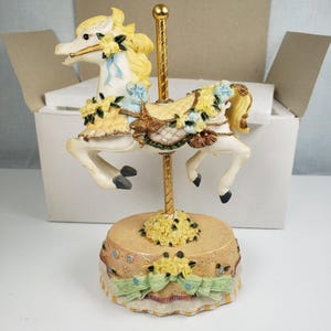 May include: A white carousel horse with a gold pole and a yellow and white base. The horse is decorated with flowers and ribbons.