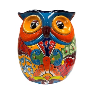 May include: A vibrantly painted ceramic owl figurine. The owl features a blue head, orange eyes, and a body adorned with colorful floral and geometric patterns in red, green, yellow, and blue. The owl has a glossy finish.