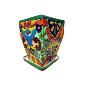 May include: A square ceramic planter with a matching saucer, featuring a vibrant, multi-colored hand-painted floral and geometric pattern in shades of blue, orange, yellow, green, and red, finished with a solid green rim and base edge.