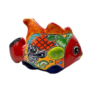 May include: A hand-painted ceramic fish figurine with a vibrant design. The fish features a red body, orange and yellow fins, and a colorful pattern of blue, green, and orange geometric shapes. The fish has a large eye and is likely a decorative item.