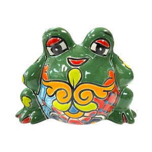 May include: A ceramic frog figurine in a vibrant green hue, adorned with colorful floral patterns in orange, blue, and yellow. The frog has large, expressive eyes and a smiling red mouth, creating a cheerful aesthetic. This decorative piece is ideal for home decor.