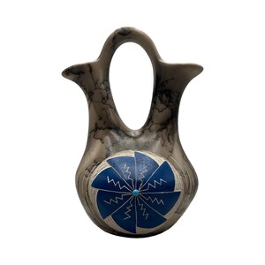 May include: A ceramic wedding vase with a smooth, light gray surface featuring dark, wispy black horsehair-style markings. The center of the vase displays a circular blue medallion with a white geometric pinwheel pattern and a small turquoise dot.