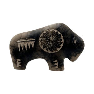 May include: A buffalo-shaped ceramic sculpture featuring a smooth, mottled gray and black finish with a horsehair-style texture. The surface is decorated with etched white geometric patterns, including a central circular sun-like motif.