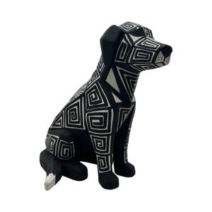 May include: A sitting dog figurine featuring a bold black and white geometric pattern of interlocking squares and spirals covering its entire body, with solid black ears and a white tip on its tail, presented in a clear, high-contrast design.