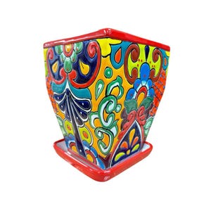 May include: A square ceramic planter with a matching saucer, featuring a vibrant hand-painted pattern in yellow, red, blue, green, and orange. The design includes intricate floral and scroll motifs covering the exterior surfaces of the pot.
