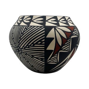 May include: A rounded ceramic pot featuring a wide opening and a tapered base. The exterior surface is decorated with intricate geometric patterns in black, white, and terracotta red, including fine line work and bold, angular shapes.