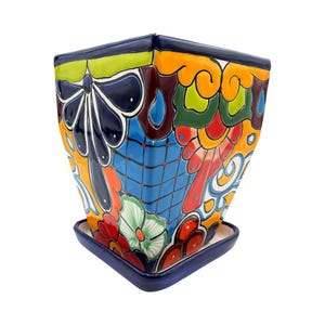 May include: A square ceramic planter with a matching saucer, featuring a vibrant hand-painted design in shades of dark blue, orange, red, green, and yellow. The exterior displays intricate floral patterns, geometric grids, and scrollwork.