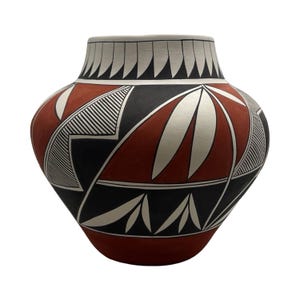 May include: A rounded ceramic vessel featuring a matte finish with a geometric pattern in black, white, and terracotta red. The design includes repeating triangular motifs around the neck and stylized leaf shapes integrated into the body.