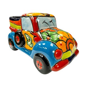 May include: A colorful ceramic truck planter with a vibrant, abstract design. The truck features a blue body, black tires, and a bed with rainbow stripes. The hood and roof are decorated with orange, green, and yellow patterns. The windshield is light blue.