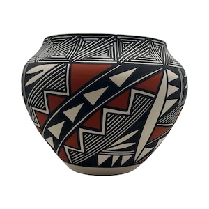 May include: A rounded ceramic pot featuring a complex geometric pattern in black, white, and terracotta red. The design includes repeating triangles, zig-zag lines, and parallel stripes covering the entire exterior surface of the vessel.