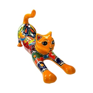 May include: A ceramic cat figurine in a stretching pose. The cat has an orange body and head with black eyes and a smiling expression. The back and sides are decorated with colorful patterns in red, blue, green, and yellow.
