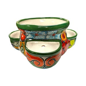 May include: A multi-tiered ceramic planter with a vibrant, hand-painted design. The planter features a large central bowl and several smaller side compartments. The color palette includes green, blue, orange, and red, with floral and swirl patterns.
