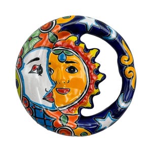 May include: A ceramic sun and moon wall hanging. The sun is orange and yellow, and the moon is white. The design includes blue, red, and green floral accents. The outer ring is dark blue with white stars and yellow swirls.