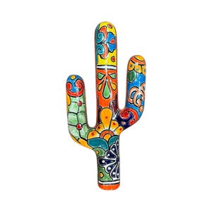 May include: A colorful ceramic cactus sculpture with a vibrant hand-painted design. The cactus features a variety of colors, including orange, yellow, blue, and green, with intricate floral and geometric patterns. The sculpture is a decorative item.