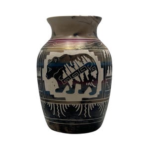 May include: A decorative ceramic vase featuring a matte finish with a central black bear silhouette. The surface displays horizontal bands of deep purple, blue, and gold, accented by intricate white geometric patterns and fine etched lines.