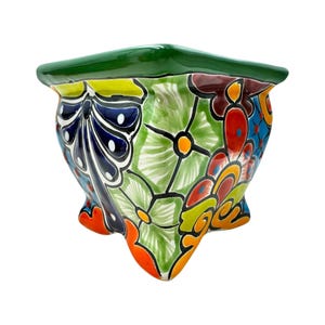 May include: A colorful, hand-painted ceramic planter with a green rim and a unique, three-footed design. The planter features a vibrant floral pattern in shades of blue, green, yellow, orange, and red, adding a touch of artistry to any space.